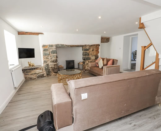 Cosy sitting room at Ty'n Lon with sofas, stone fireplace and electric log burner